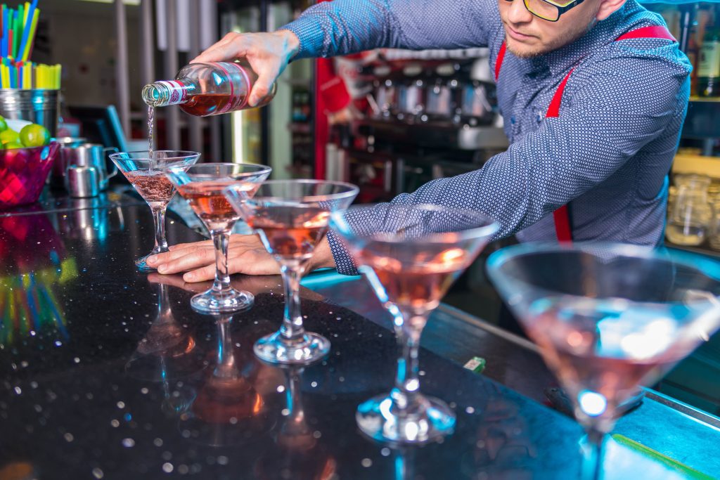 A bartender pours drinks into cocktail glasses