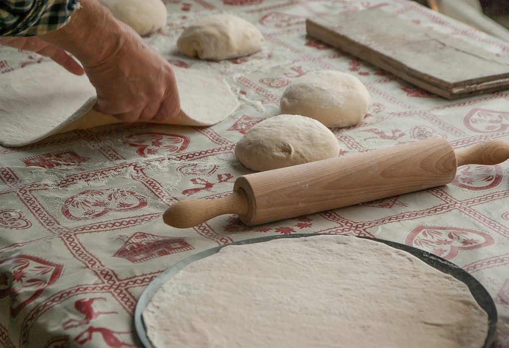 A chef rolls out dough to make pizza